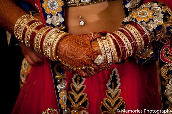 The bride puts traditional red and cream bangles on her wrists for the Indian wedding ceremony.