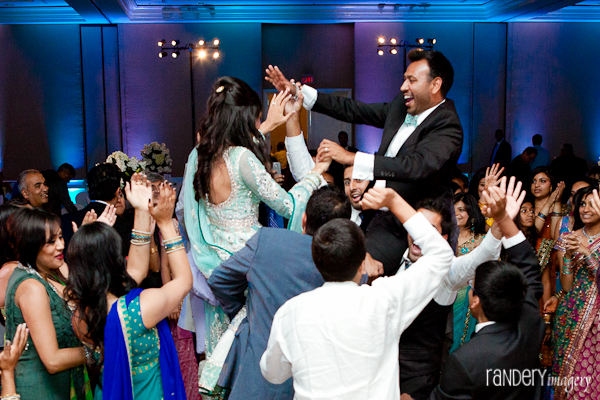 An Indian bride and groom are hoisted in the air at their Indian wedding reception.