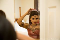 To prepare for her fabulous Indian wedding, this bride gets her hair and makeup done and she slips into a beautiful bright red lengha.