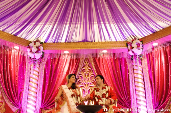 An indian bride and groom sit under a modern mandap.