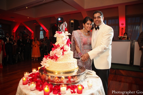 An indian bride and groom pose with their indian wedding cake in white and red.