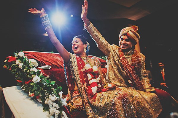 An Indian bride and groom wave goodbye to family at Indian wedding ceremony.