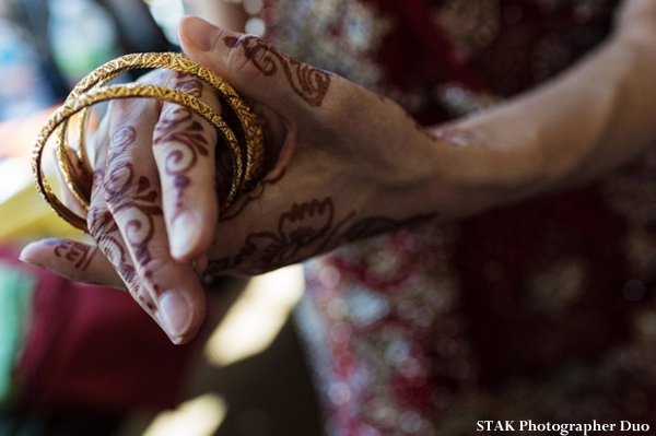 Indian bride puts on gold churis on her hands with bridal mehndi
